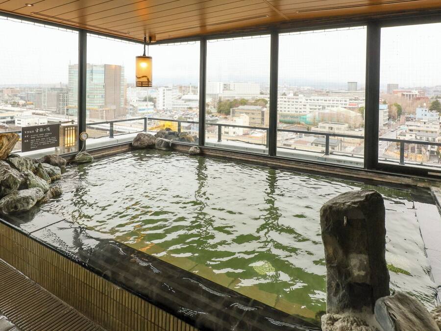 A hot spring bath with a city view, large windows, and wooden beams.