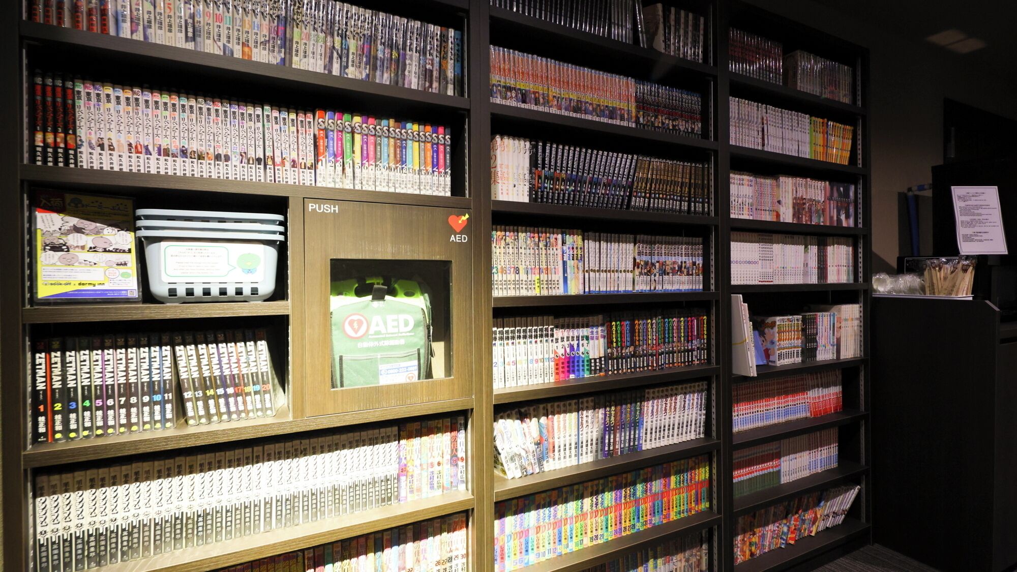 A library with bookshelves filled with books and a push box with AED instructions.