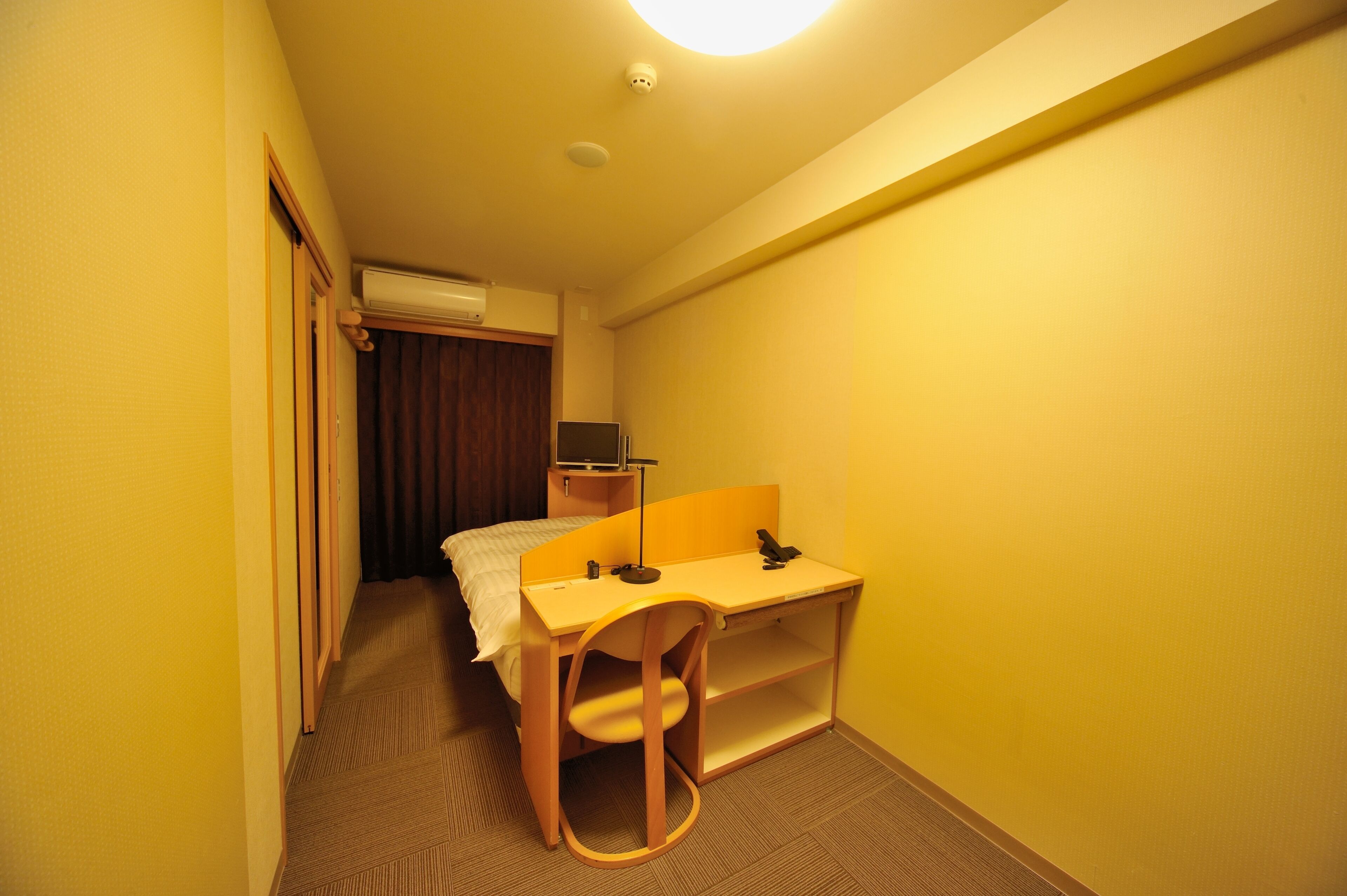 A compact hotel room with a single bed, a desk, and a chair.