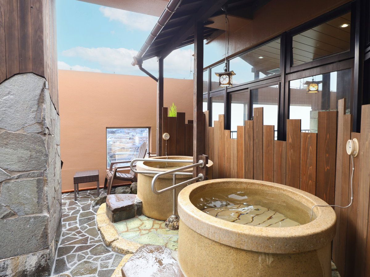 A stone-tiled outdoor area with two stone hot tubs, a wooden fence, and a stone wall.