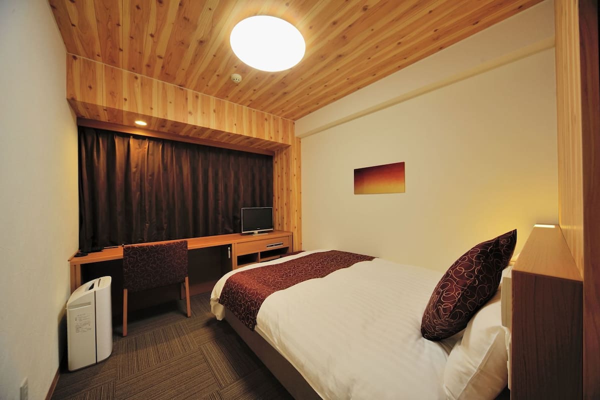 A hotel room with a wooden ceiling, a bed with patterned bedding, a desk with a television, and a wall-mounted picture.
