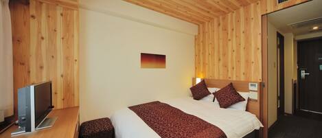 A hotel room with a wooden ceiling, a bed with a patterned bedspread, a bedside table with a flat-screen TV, and a small bench.