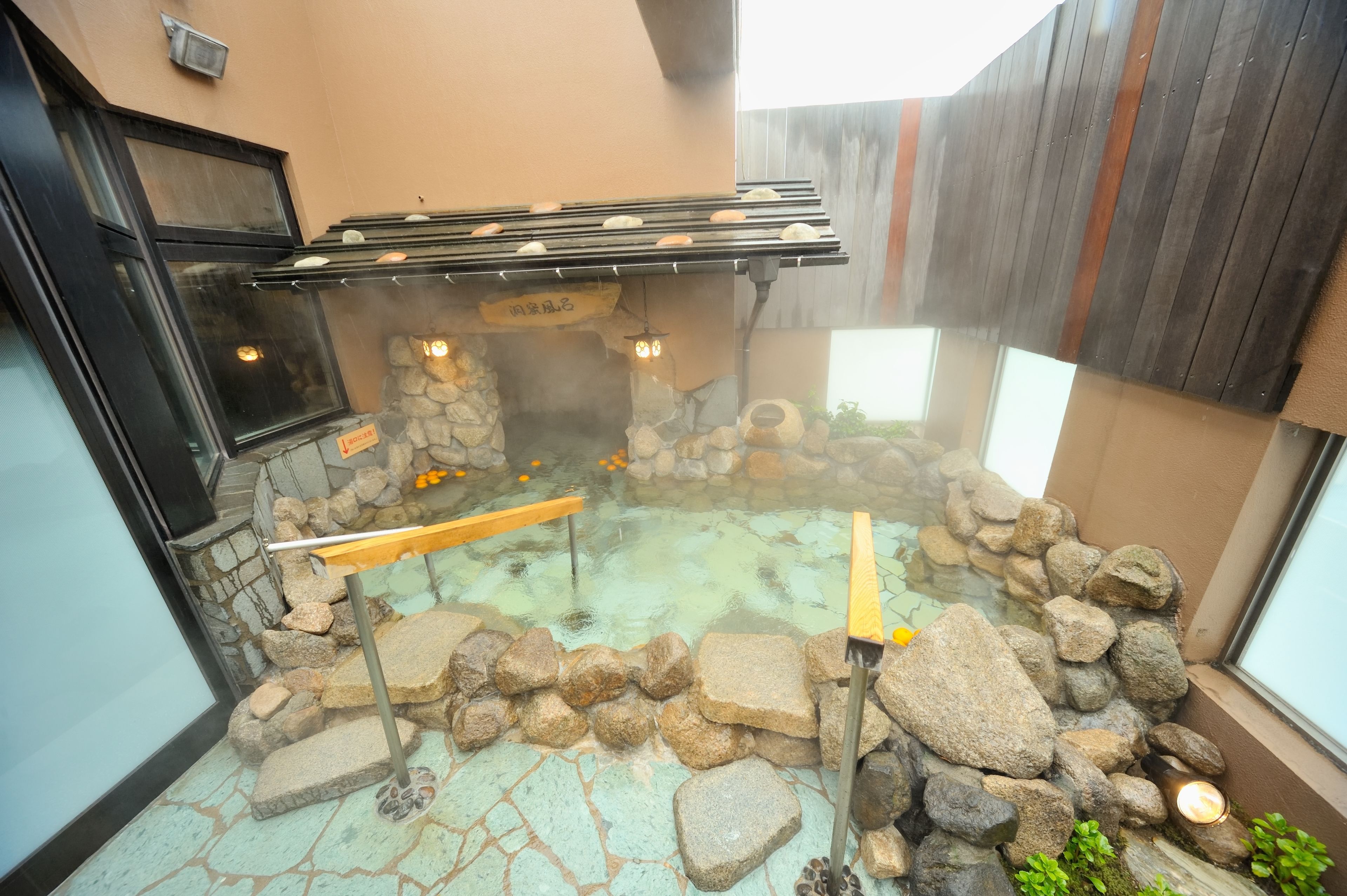 A hot spring area with stone walls, wooden benches, and a tiled floor.