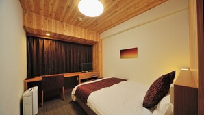 A hotel room with a wooden ceiling, a bed with a patterned pillow, a desk with a television, and a small white appliance.
