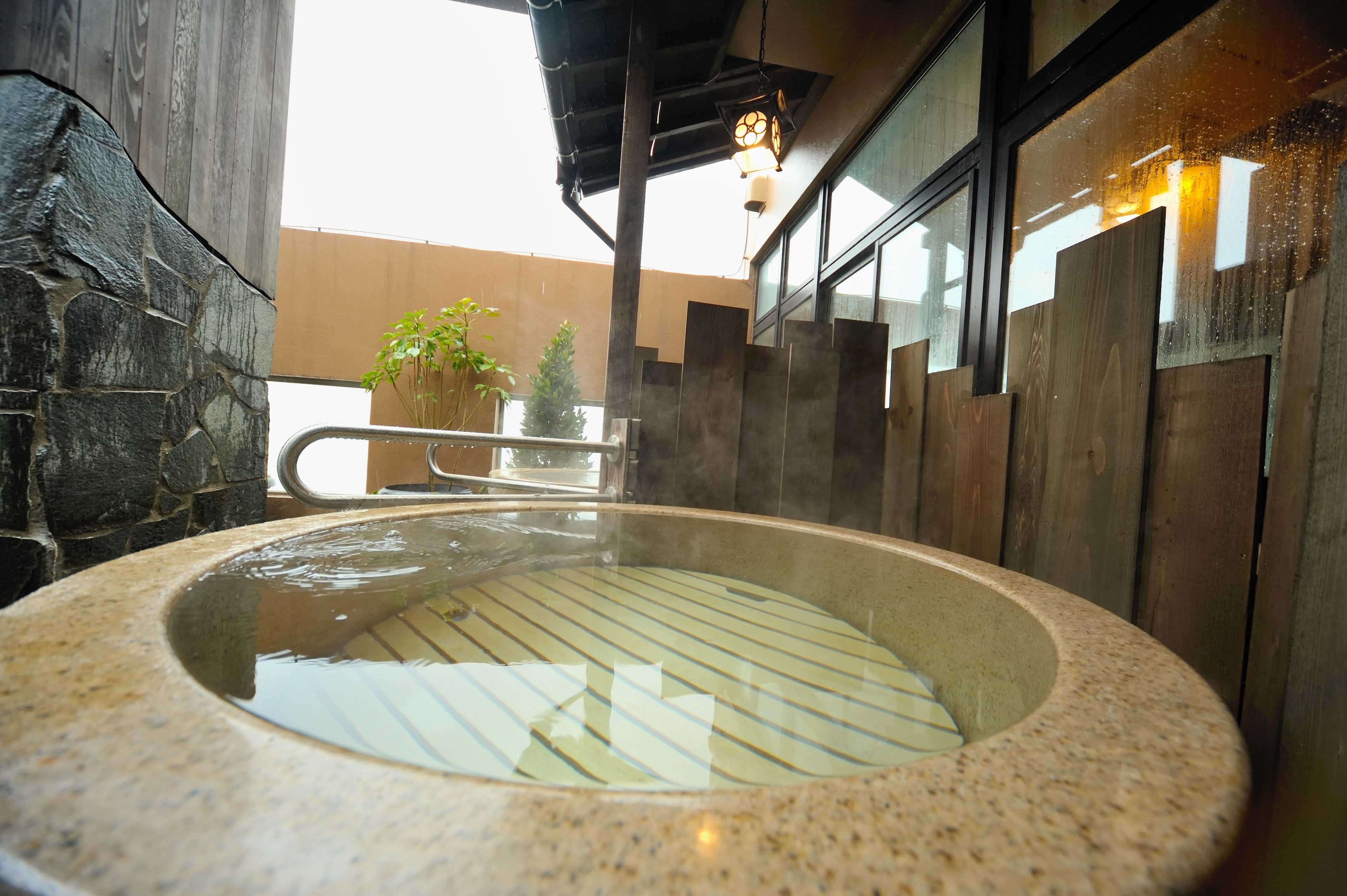 Un baño de aguas termales con pared de piedra, paneles de madera, barandilla metálica y una lámpara colgante.