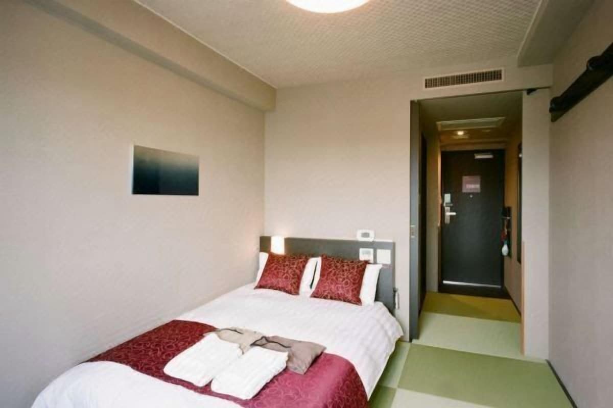 A hotel room with a bed, a headboard, a door, and a small wall-mounted item.