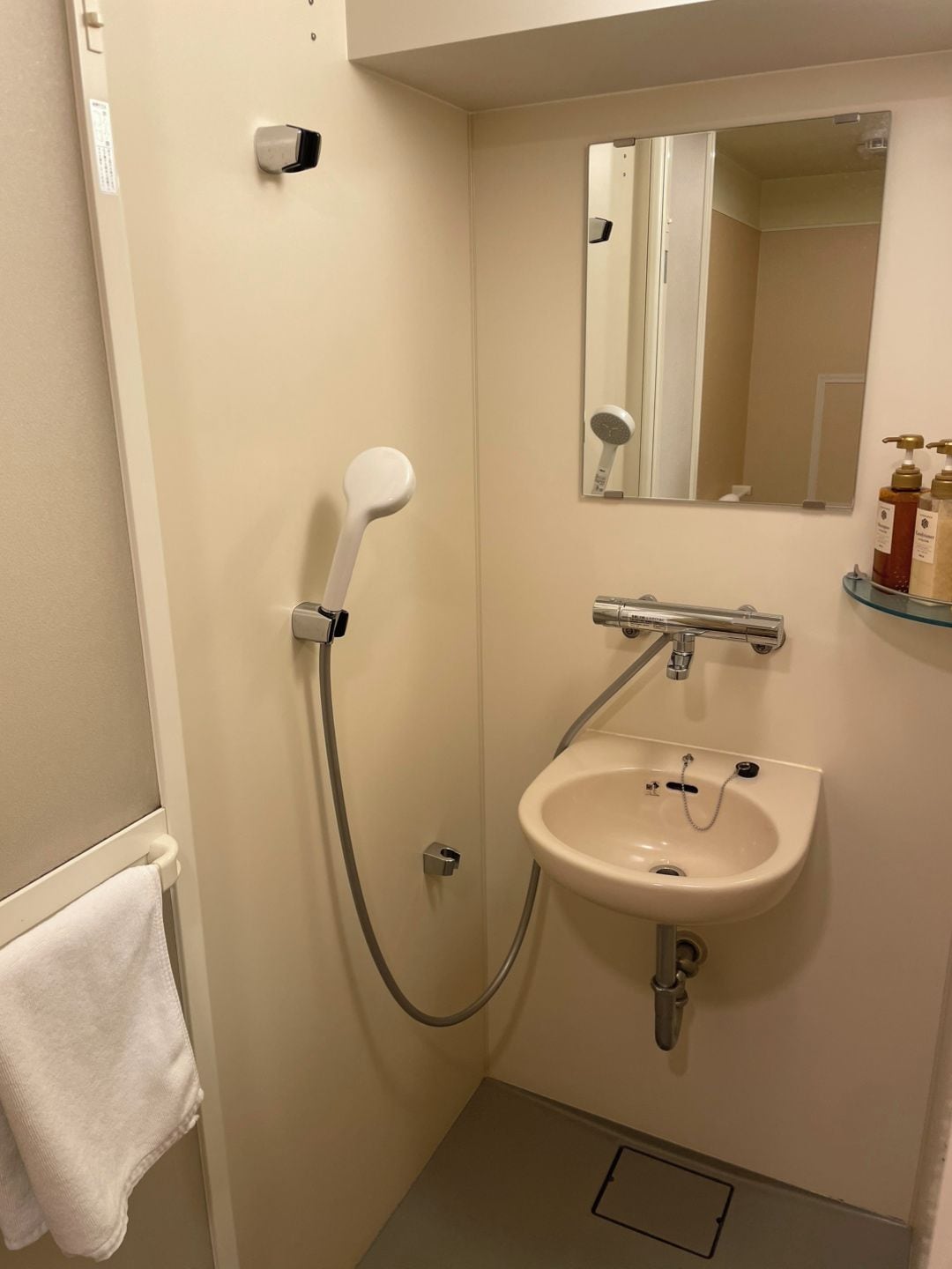 A small bathroom with a shower, sink, and mirror.