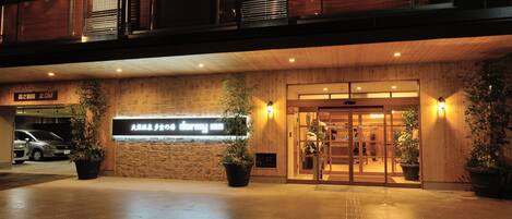 Entrada de hotel con fachada de madera, un letrero que indica un espacio de estacionamiento para 2.0 metros y plantas en macetas.