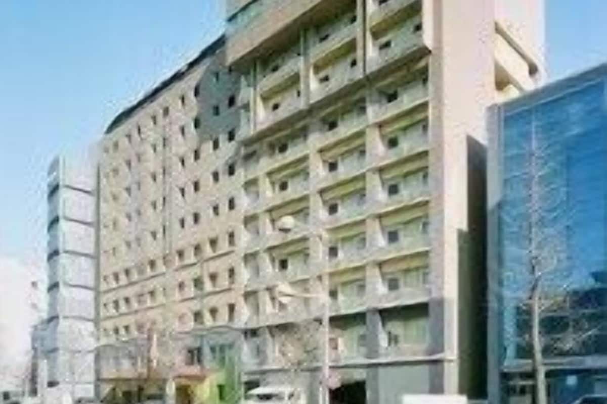 A multi-story hotel with a modern architectural design, featuring a prominent central entrance and a parking area in front.