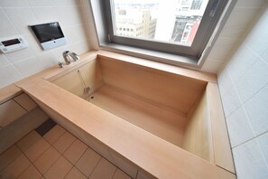A modern bathroom with a large bathtub, a window with a city view, and a digital thermostat on the wall.