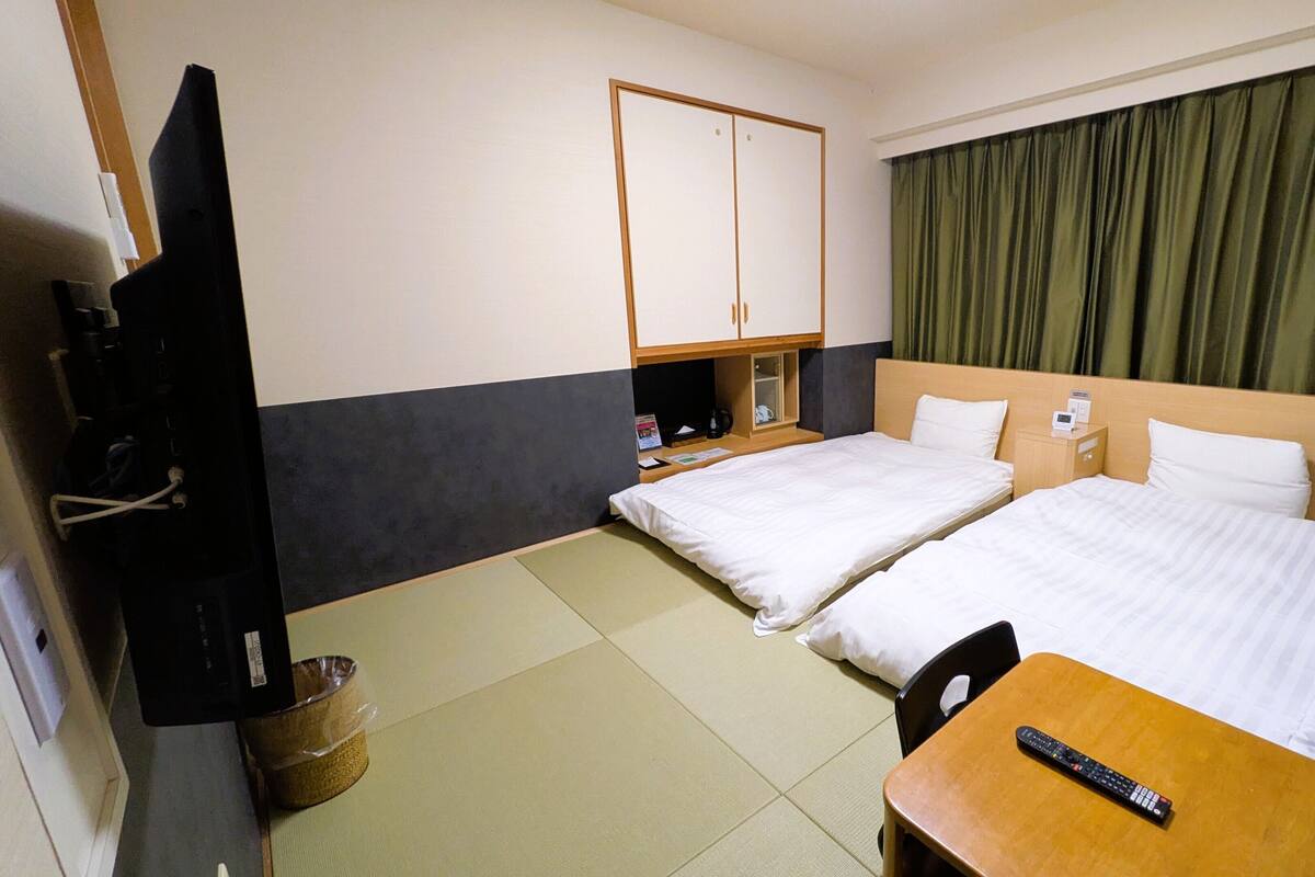 A hotel room with two beds, a TV, a small table, and a cabinet.