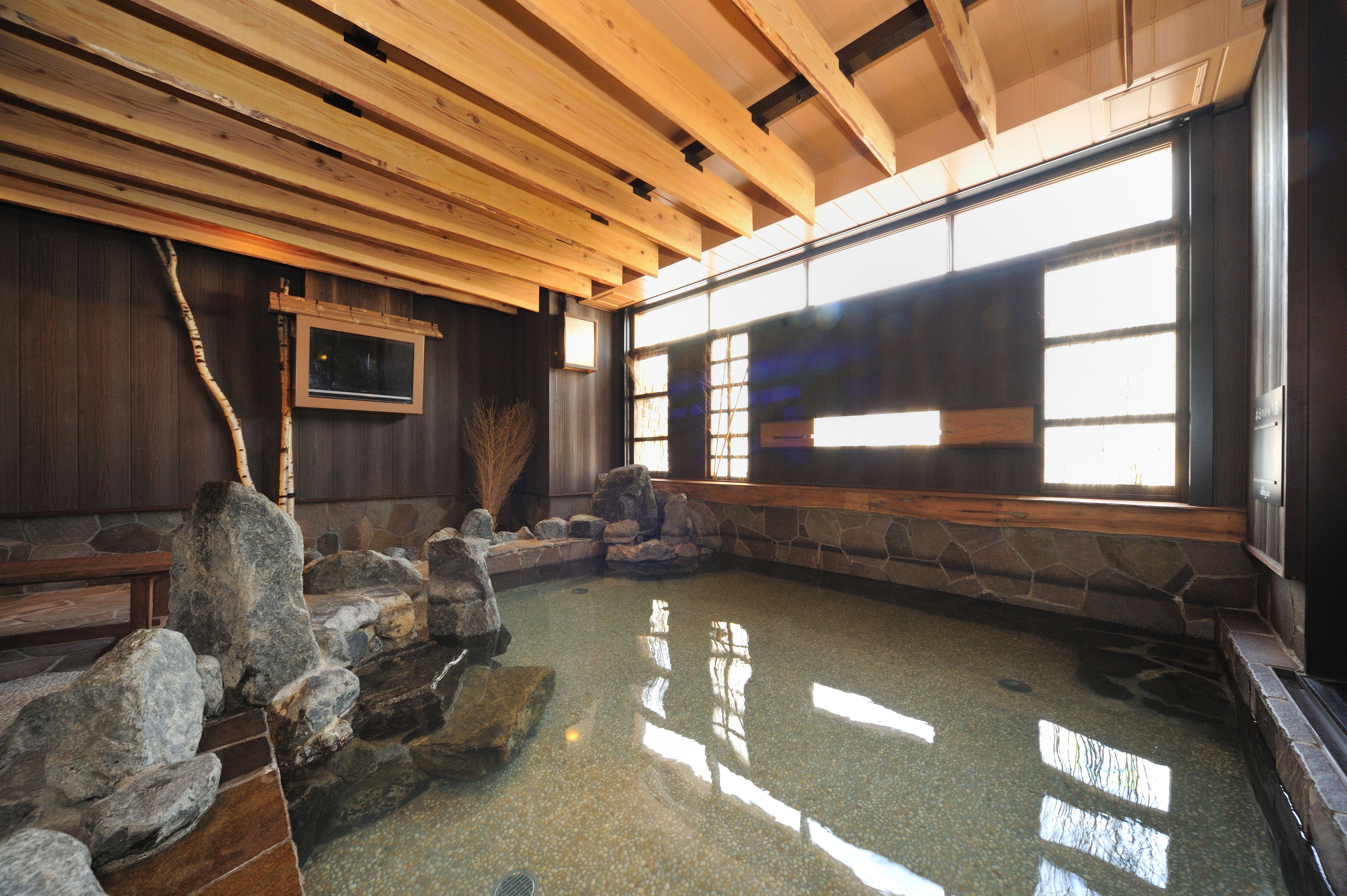 Una habitación japonesa tradicional con suelo de tatami, una fuente de agua de piedra y ventanas amplias.