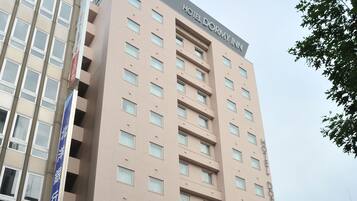 A multi-story hotel with a sign reading "Hotel Dormy Inn" and a visible entrance.