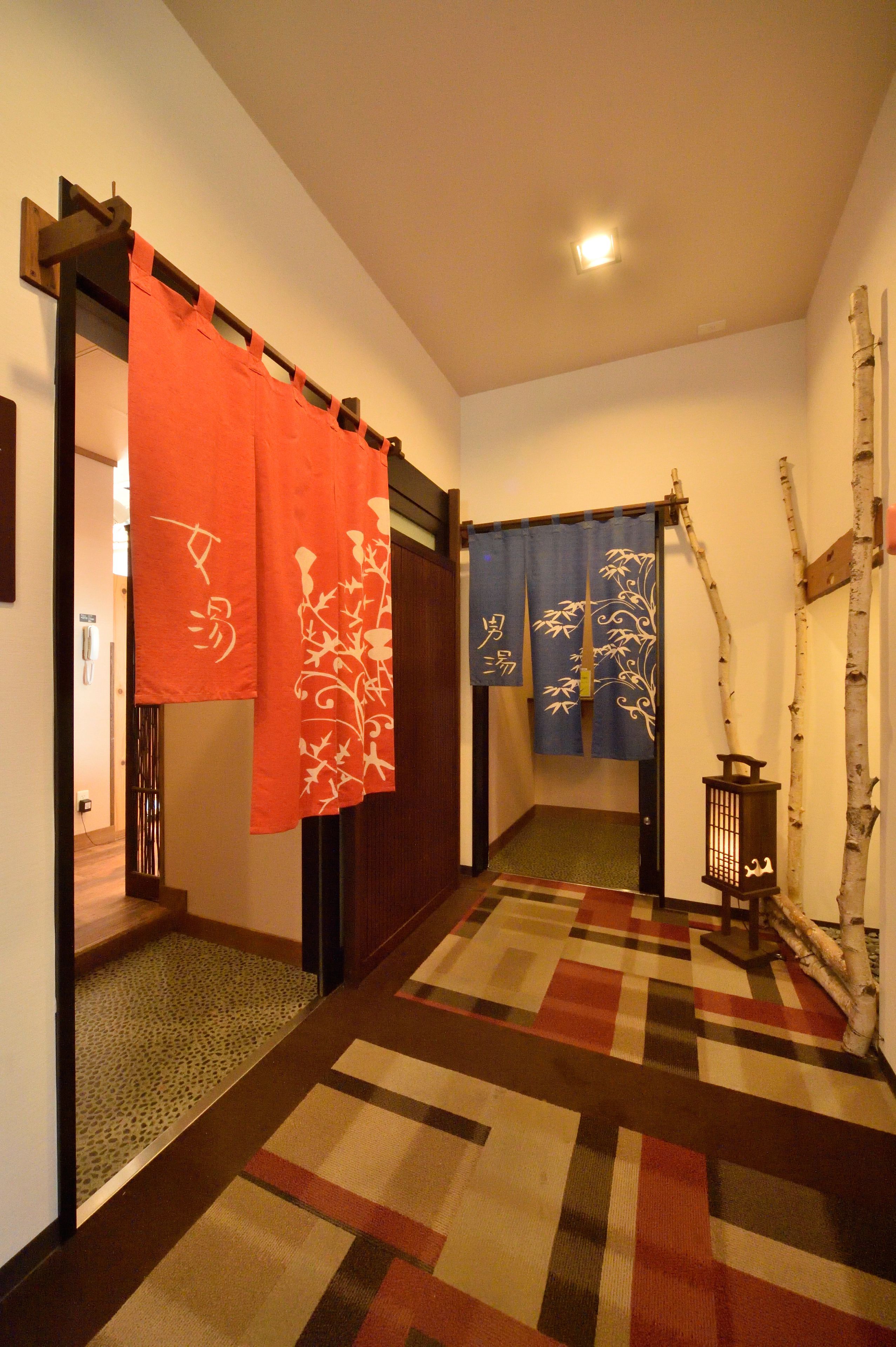 A hallway with a patterned carpet, a wooden door, and a traditional Japanese room divider with red and blue curtains.