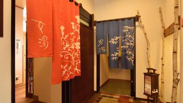 A hallway with a patterned carpet, a wooden door, and a traditional Japanese room divider with red and blue curtains.