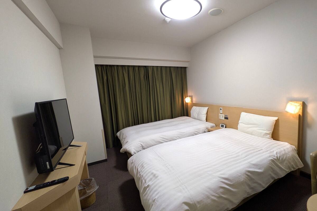 A hotel room with two beds, a TV, a desk, and a chair.