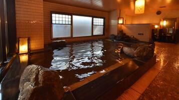 A traditional Japanese onsen with a stone bath, tiled walls, and a wooden floor.