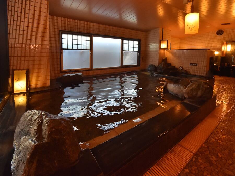 A traditional Japanese onsen with a stone bath, tiled walls, and a wooden floor.