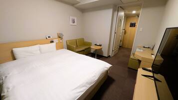 A hotel room with a bed, a desk, a chair, a small table, a TV, and a door leading to another room.