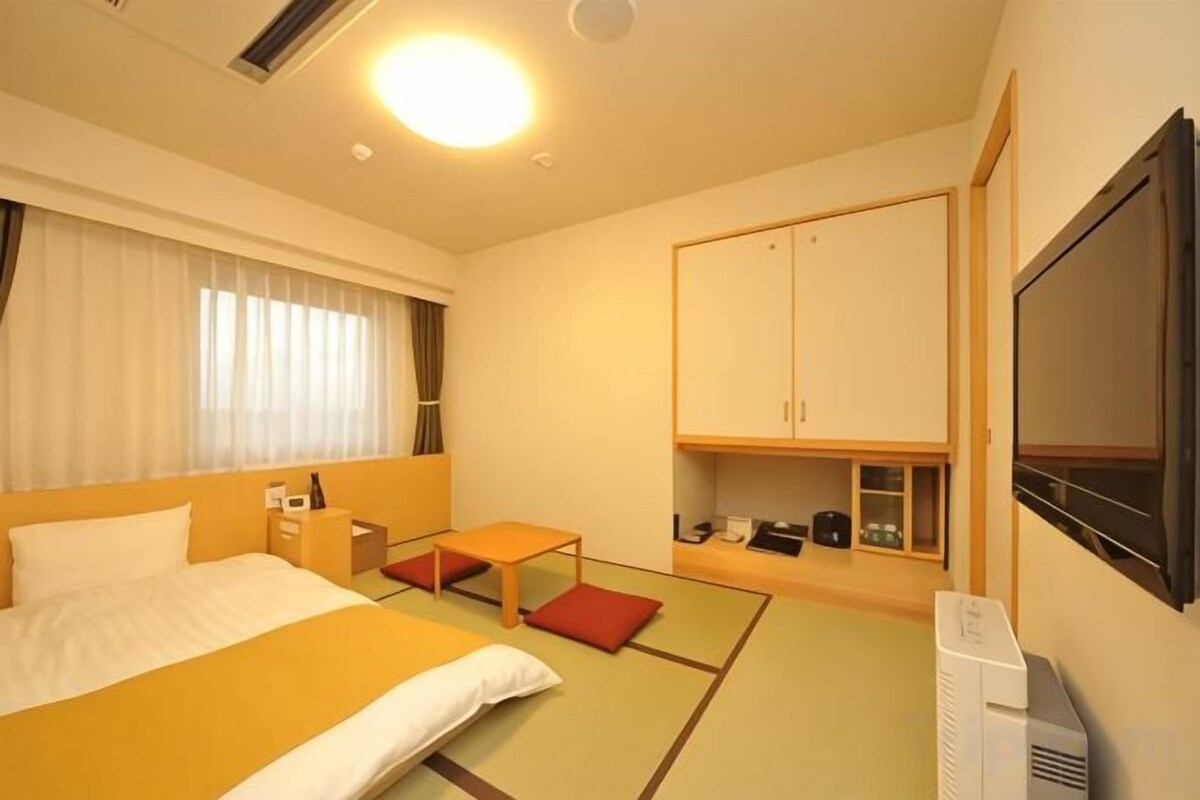 A hotel room with a bed, a desk, a chair, a television, and a wardrobe.