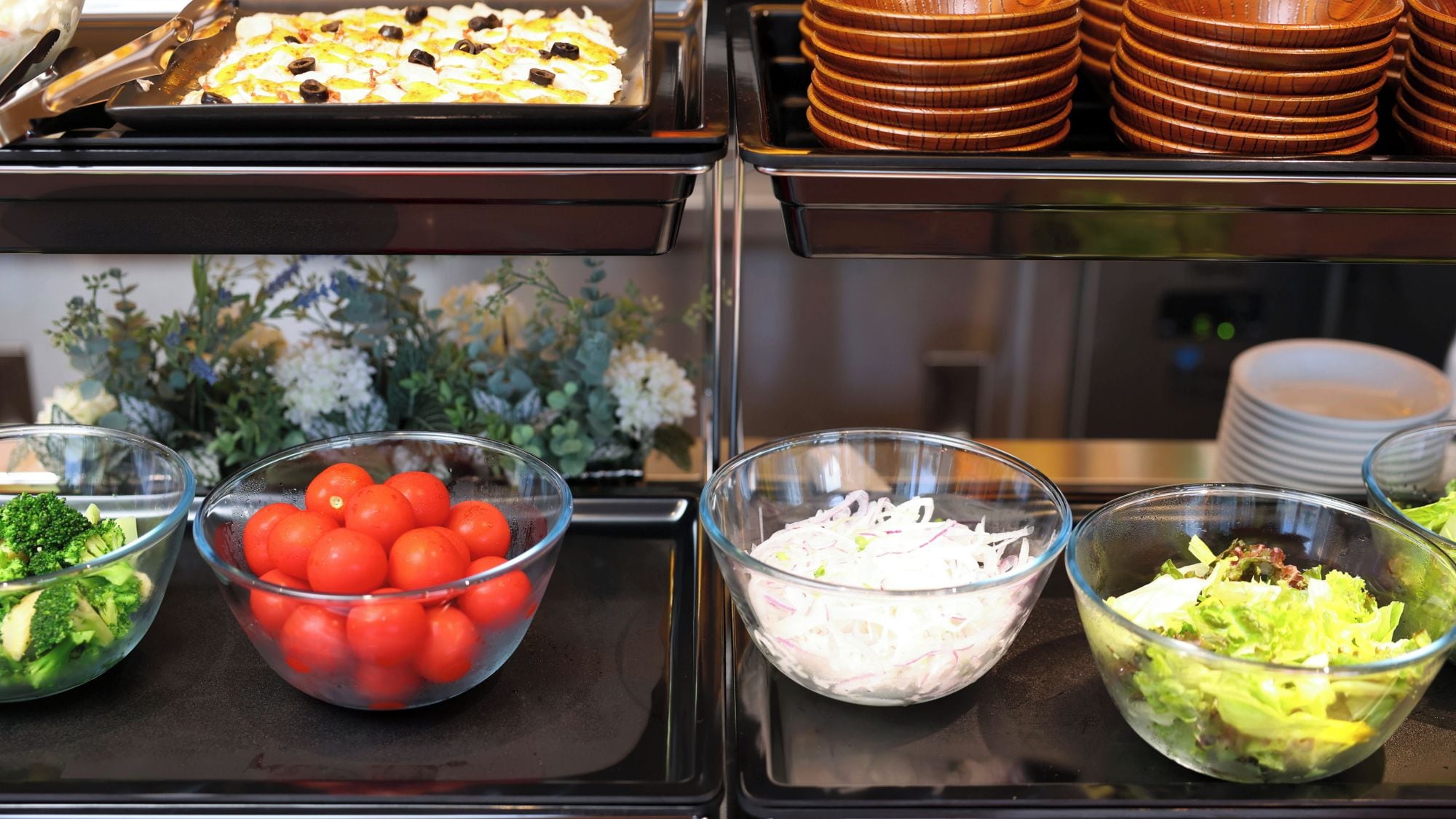 Un bufé con distintos alimentos, incluyendo brócoli, tomates cherry, cebolla picada y una ensalada.