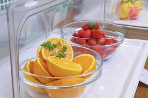 A glass display case containing bowls of sliced oranges and strawberries.
