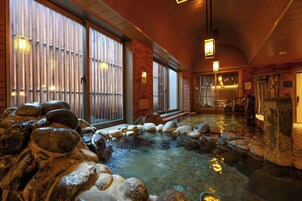 A traditional Japanese onsen with a stone bath surrounded by wooden walls and sliding doors.