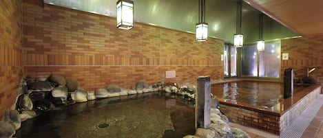 A hot spring bath area with a brick wall, stone seating, and hanging lights.
