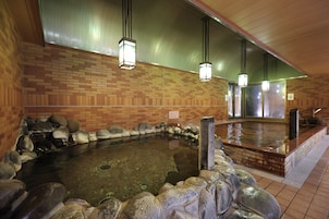 A hot spring bath area with a brick wall, stone seating, and hanging lights.