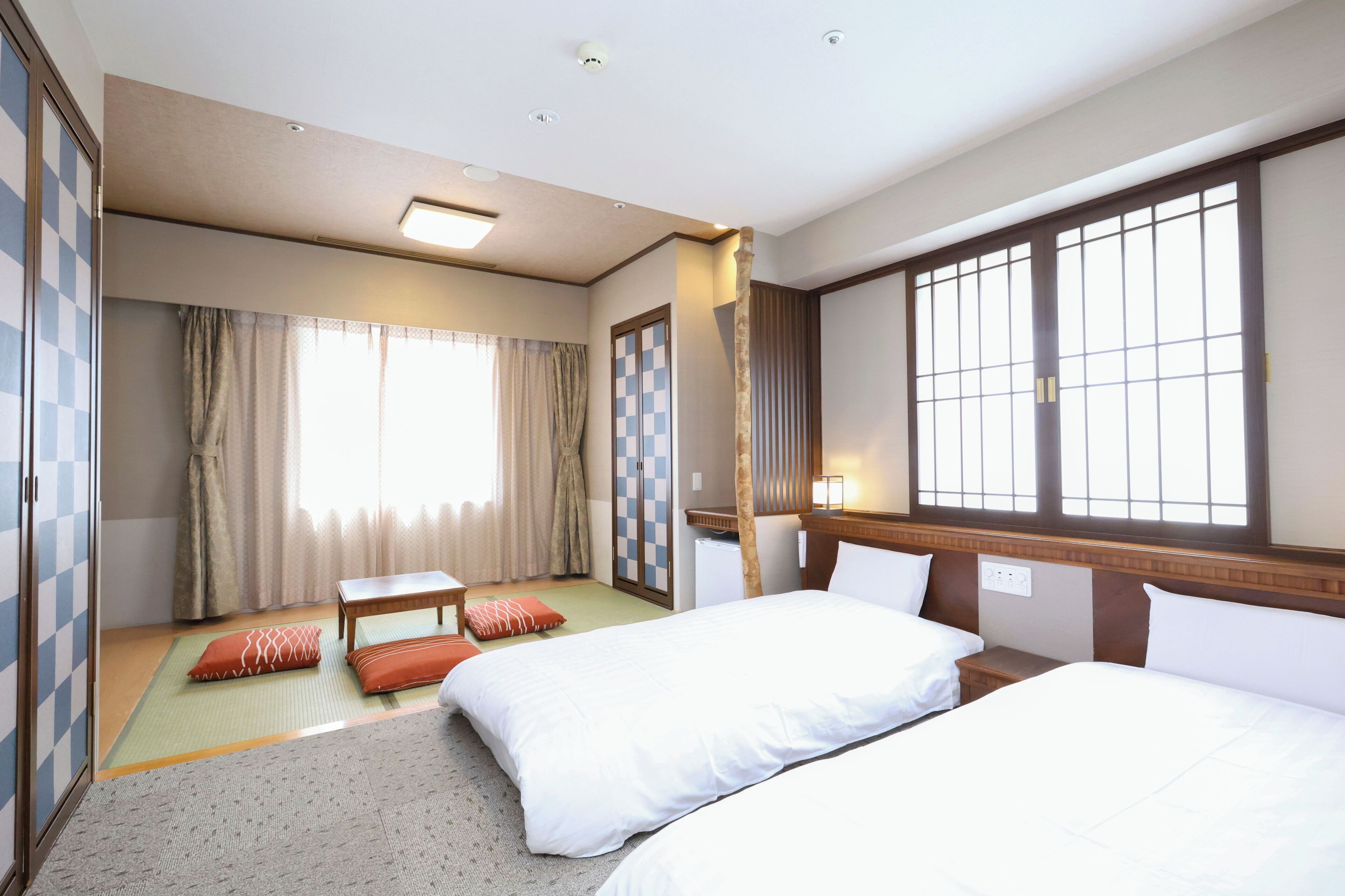 A hotel room with two beds, a small table, a sofa, a window with a view, and a wardrobe.