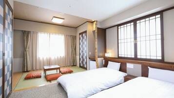 A hotel room with two beds, a small table, a sofa, a window with a view, and a wardrobe.