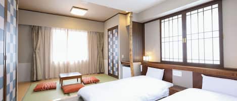 A hotel room with two beds, a small table, a sofa, a window with a view, and a wardrobe.