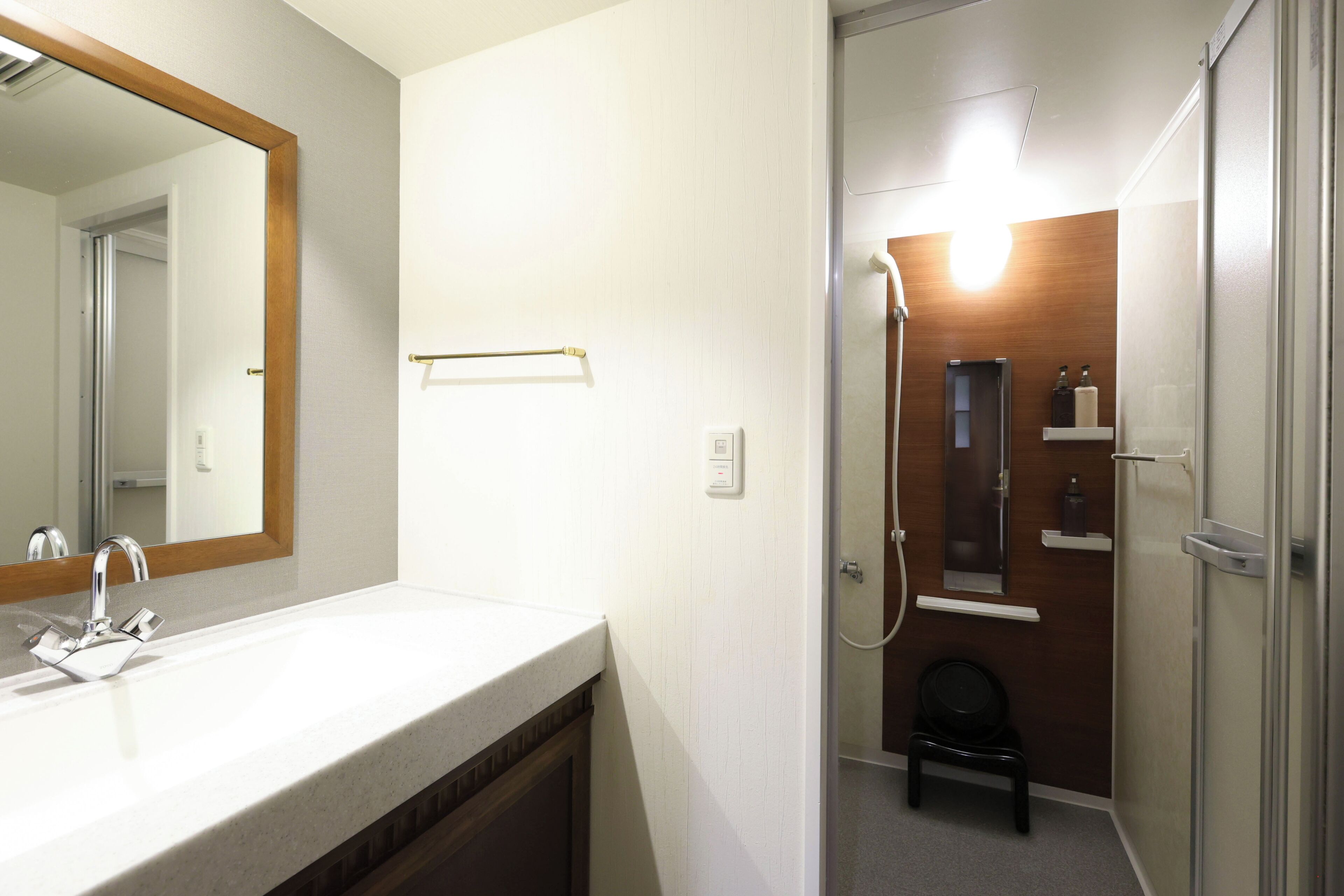 Une salle de bain équipée d’un lavabo, d’un miroir, d’un porte-serviettes, d’une douche et d’un petit tabouret.