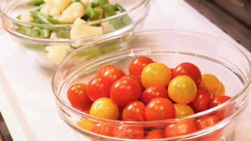 Two glass bowls on a white surface, one with cherry tomatoes and the other with a salad.