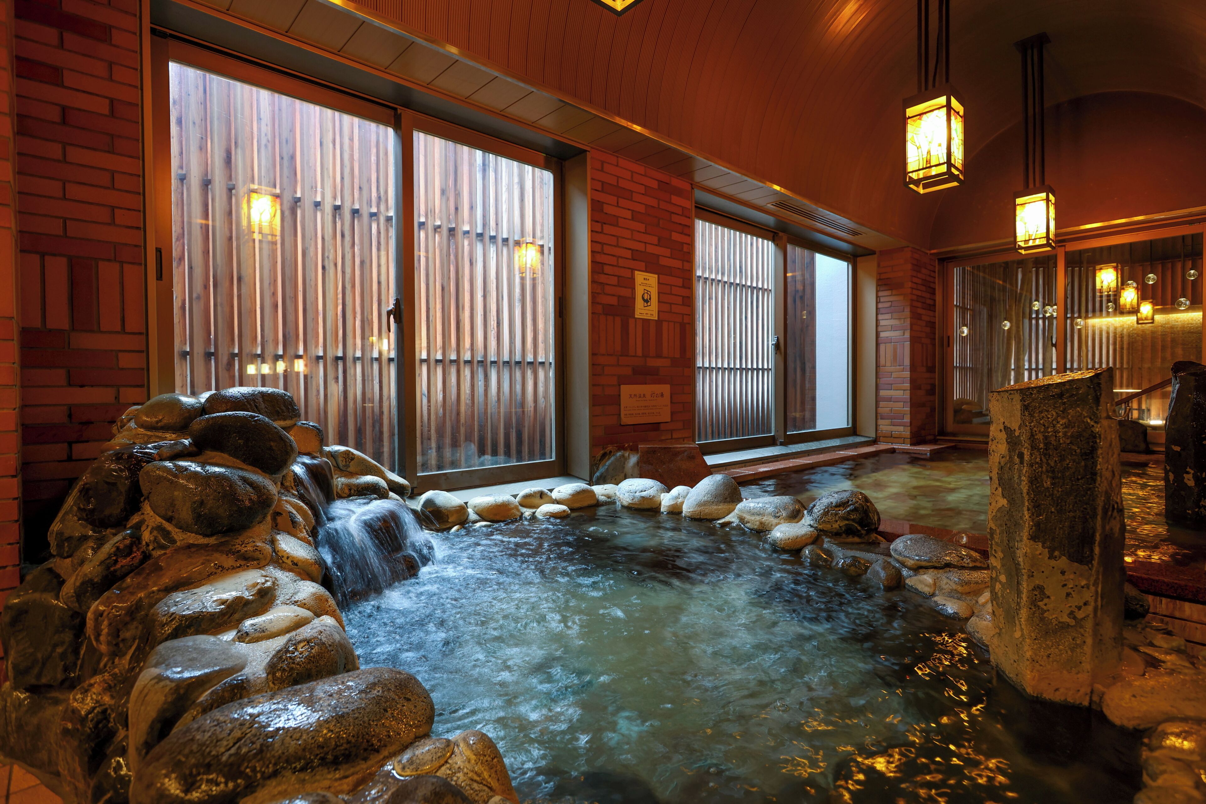 A hot spring area with a stone fountain, wooden benches, and a tiled floor.