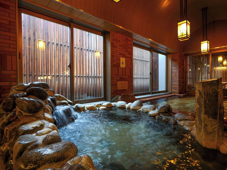 A hot spring area with a stone fountain, wooden benches, and a tiled floor.
