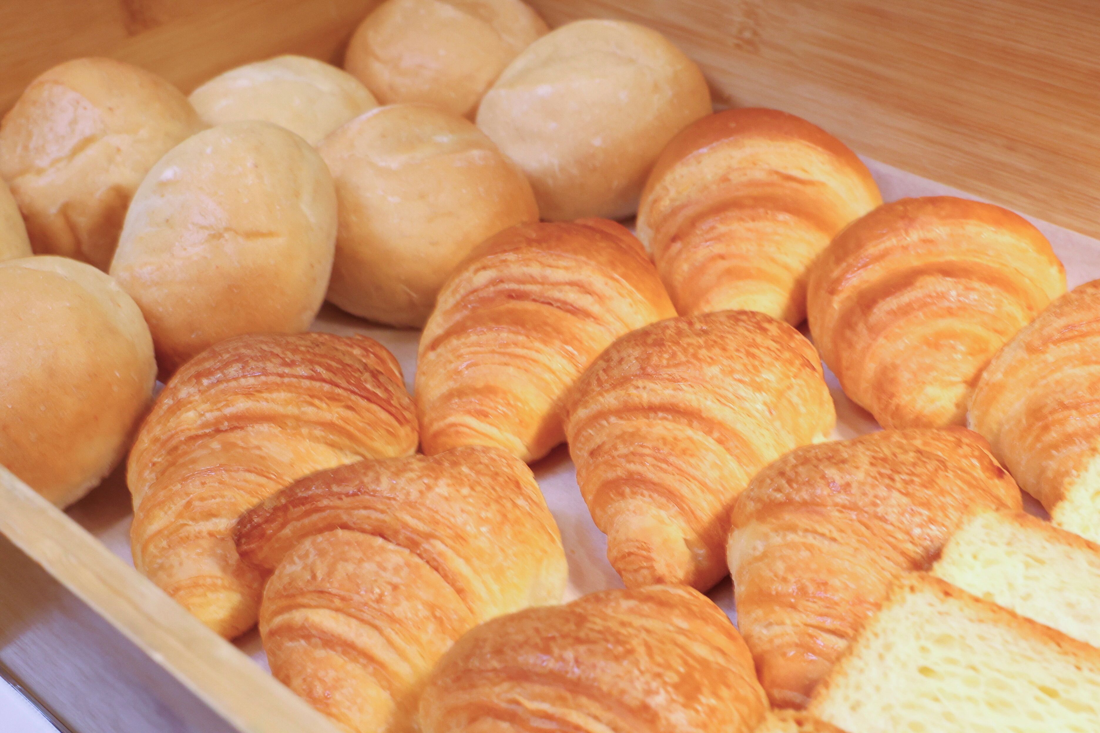 A wooden tray filled with various types of bread rolls and croissants.