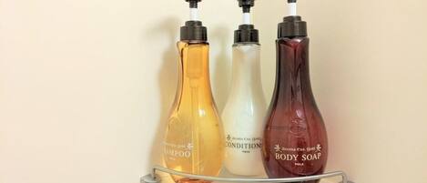 Tres botellas de champú, acondicionador y jabón de cuerpo sobre un estante de vidrio transparente.