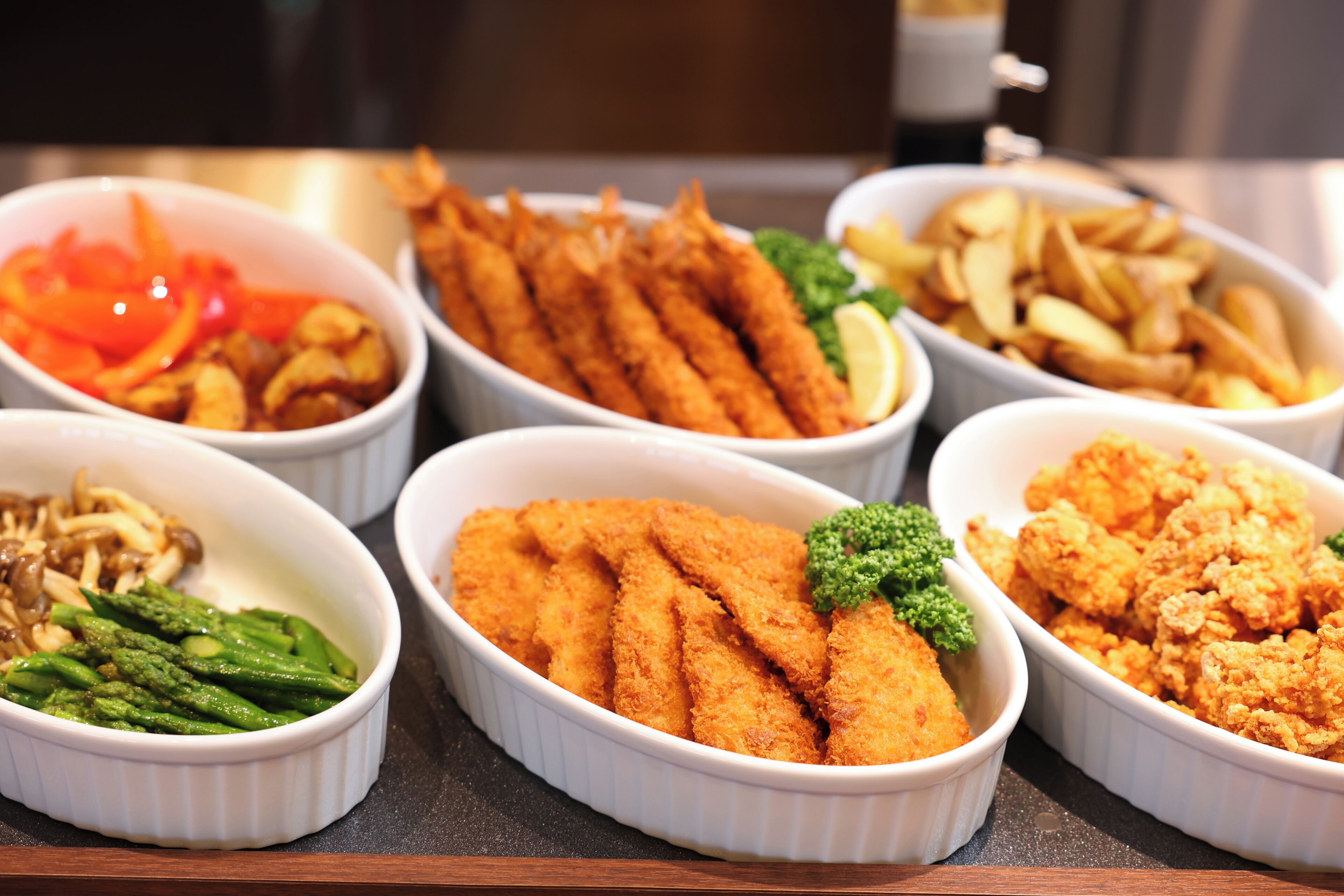 A variety of dishes including breaded fish, asparagus, and fries in white bowls.