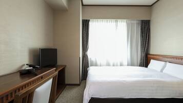 A hotel room with a bed, a desk with a television, and a window with curtains.
