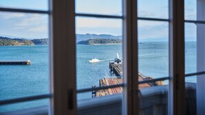 A view through a window of a coastal area with a pier, a boat, and distant mountains. - Hotel Den Haag Huis Ten Bosch (Sasebo)