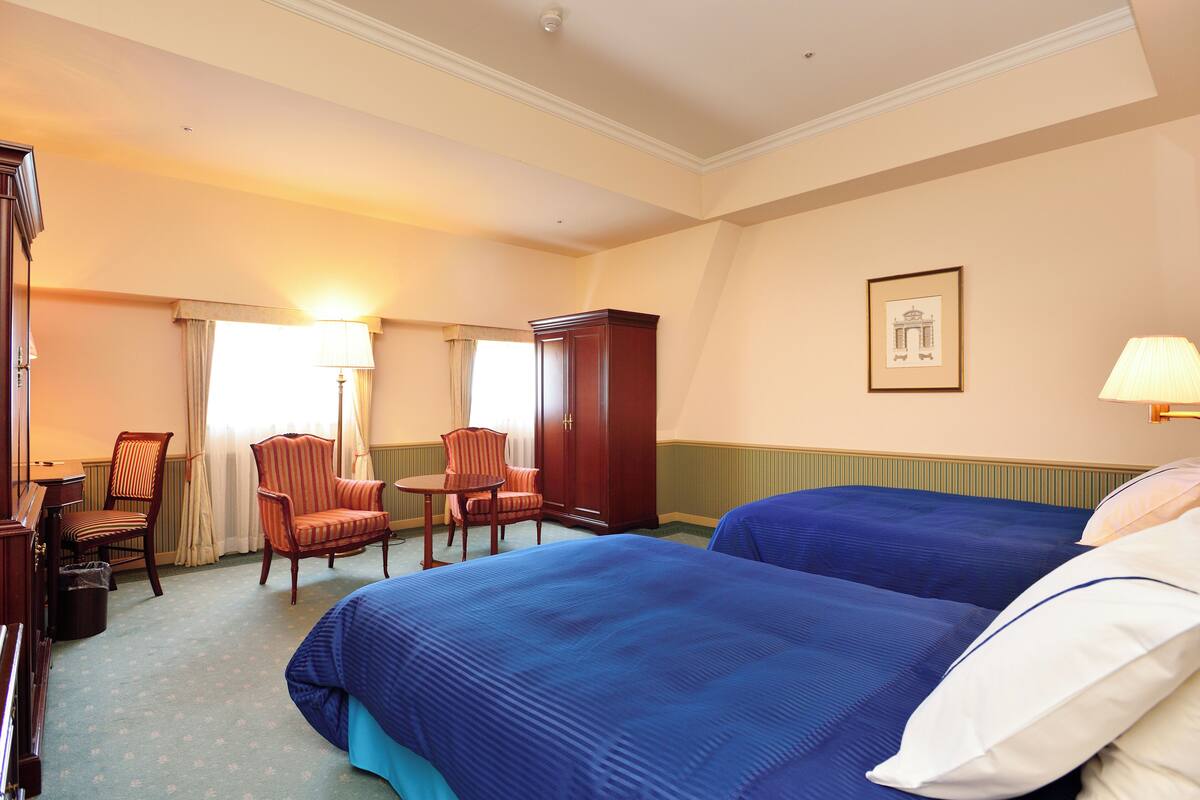 A hotel room with two beds, a desk, a chair, a wardrobe, and a framed picture on the wall.