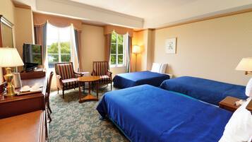 A hotel room with two beds, a desk with a lamp, a chair, a television, and a window with curtains.