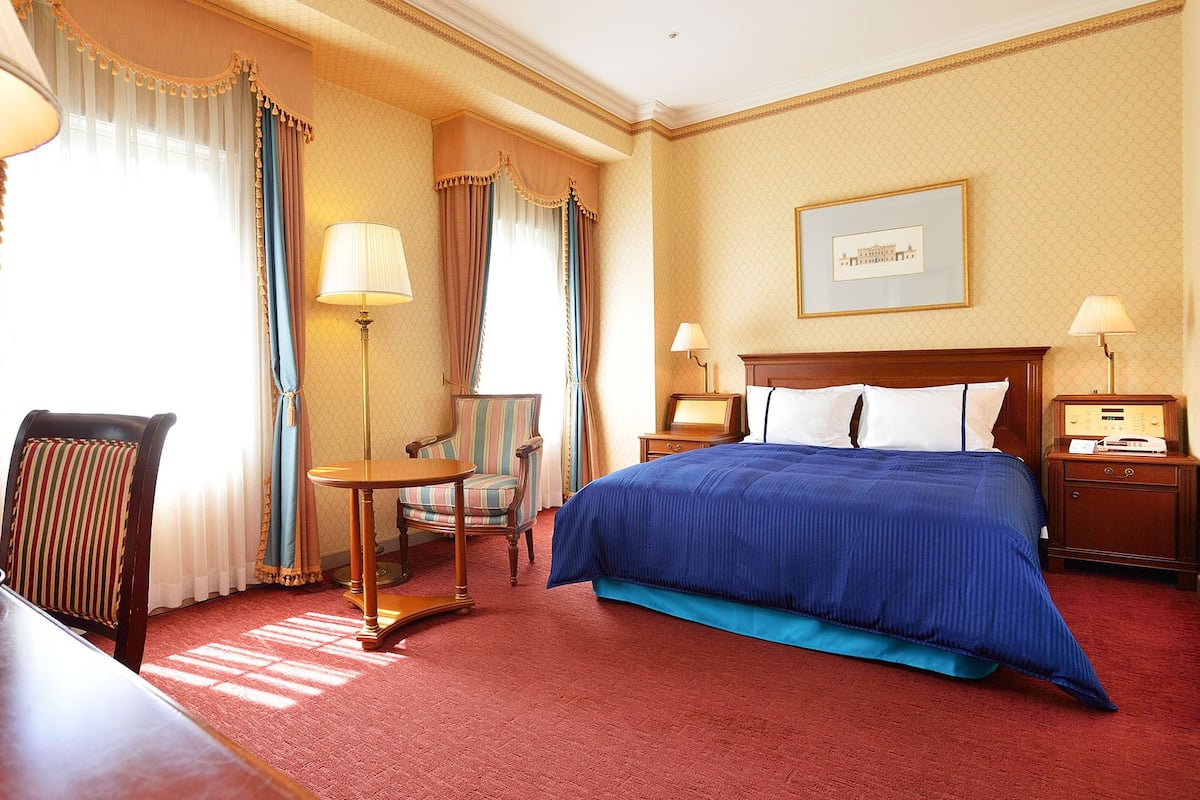 A hotel room with a bed, a chair, a desk, and a lamp.