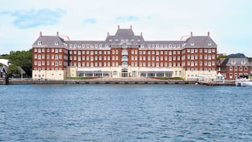 A large, historic building with multiple floors, a central entrance, and a waterfront view.