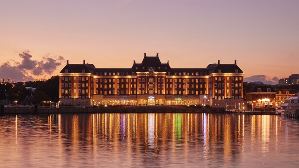 A large, illuminated hotel with multiple stories and a prominent entrance, situated by a waterfront. - Hotel Den Haag Huis Ten Bosch (Sasebo)