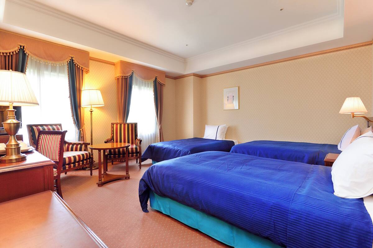 A hotel room with two beds, a desk, a chair, and lamps.