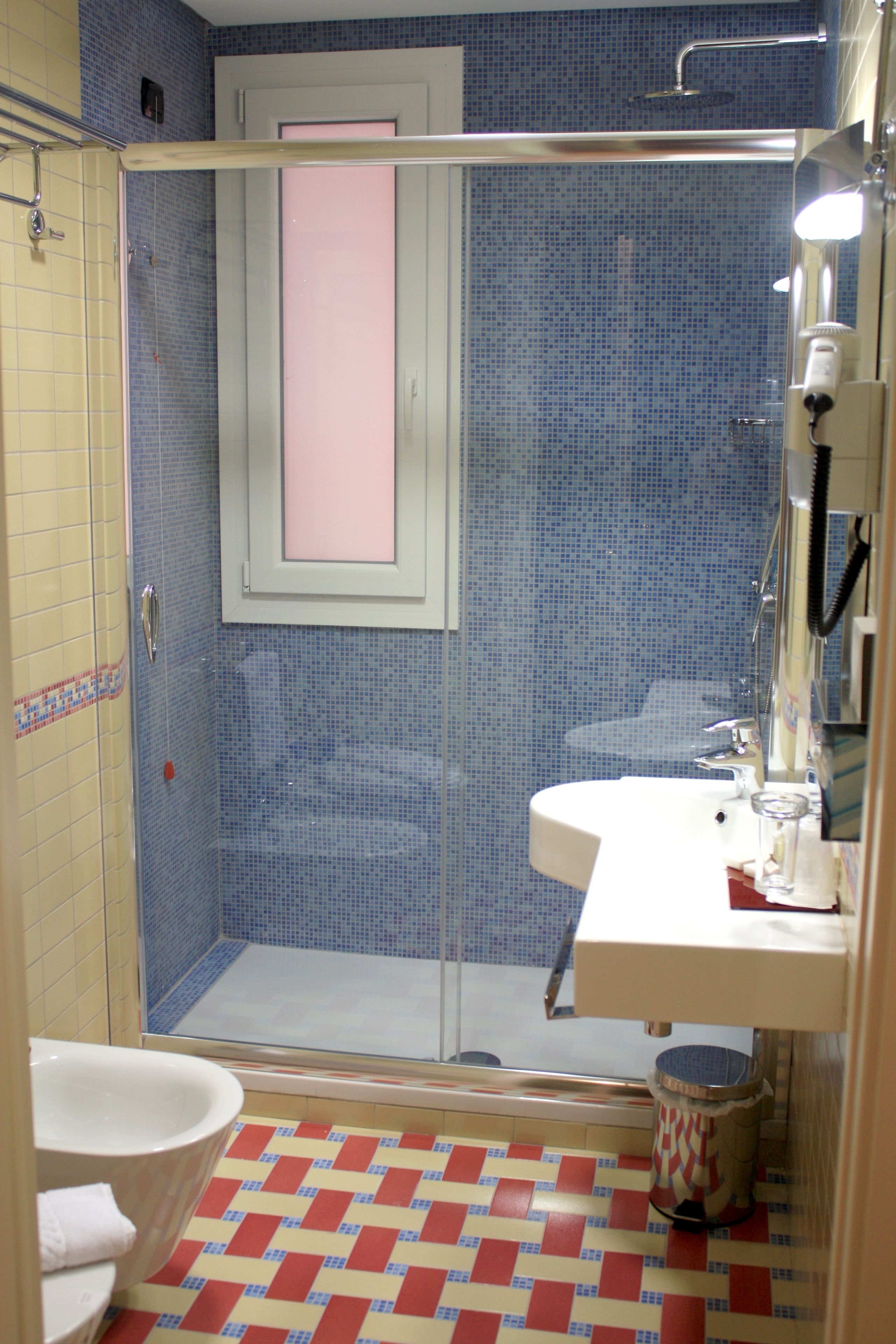 A bathroom with a shower, toilet, sink, and a tiled floor.