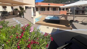 A rooftop terrace with a hot tub, outdoor seating, and a pool.