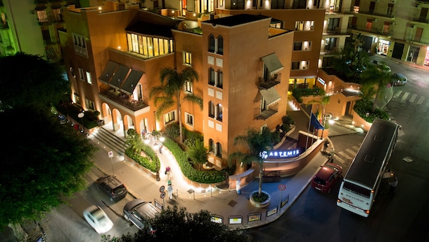 A multi-story hotel with a central courtyard, outdoor seating, and a bus stop. - Artemis Hotel (Cefalù)